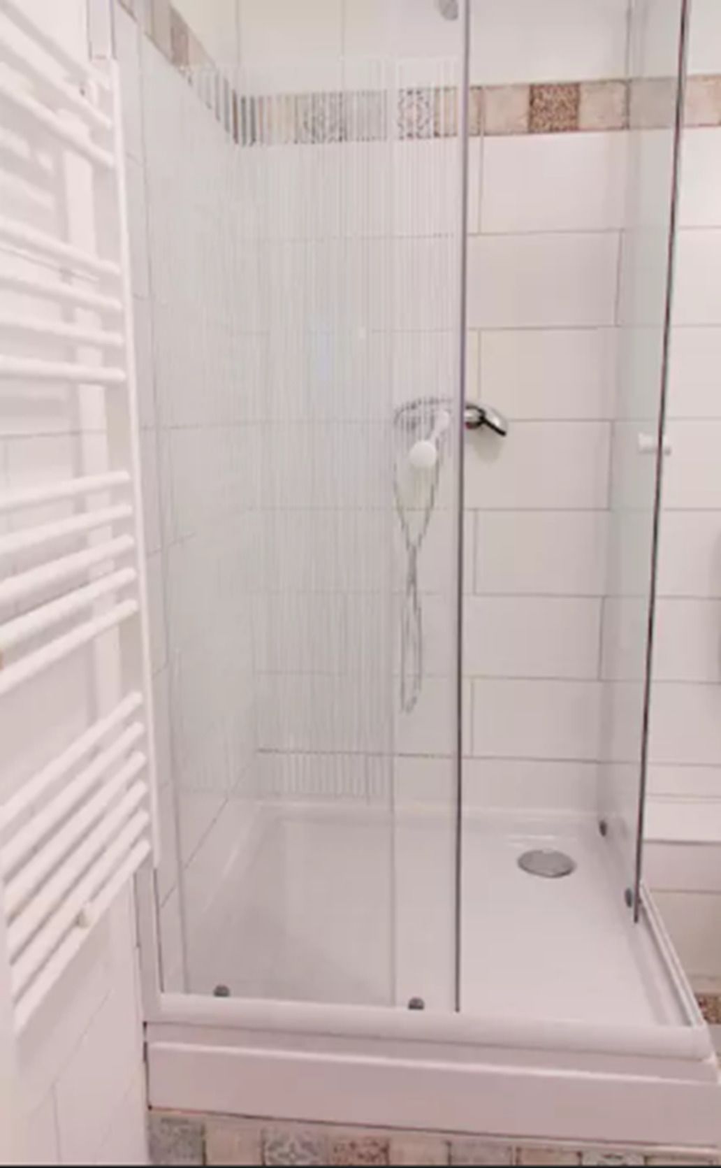 Una cabina de ducha con paredes de azulejos blancos y piso blanco.