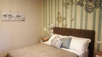 A bedroom with a bed, pillows, a nightstand, a lamp, and a wall with striped wallpaper and butterfly designs.
