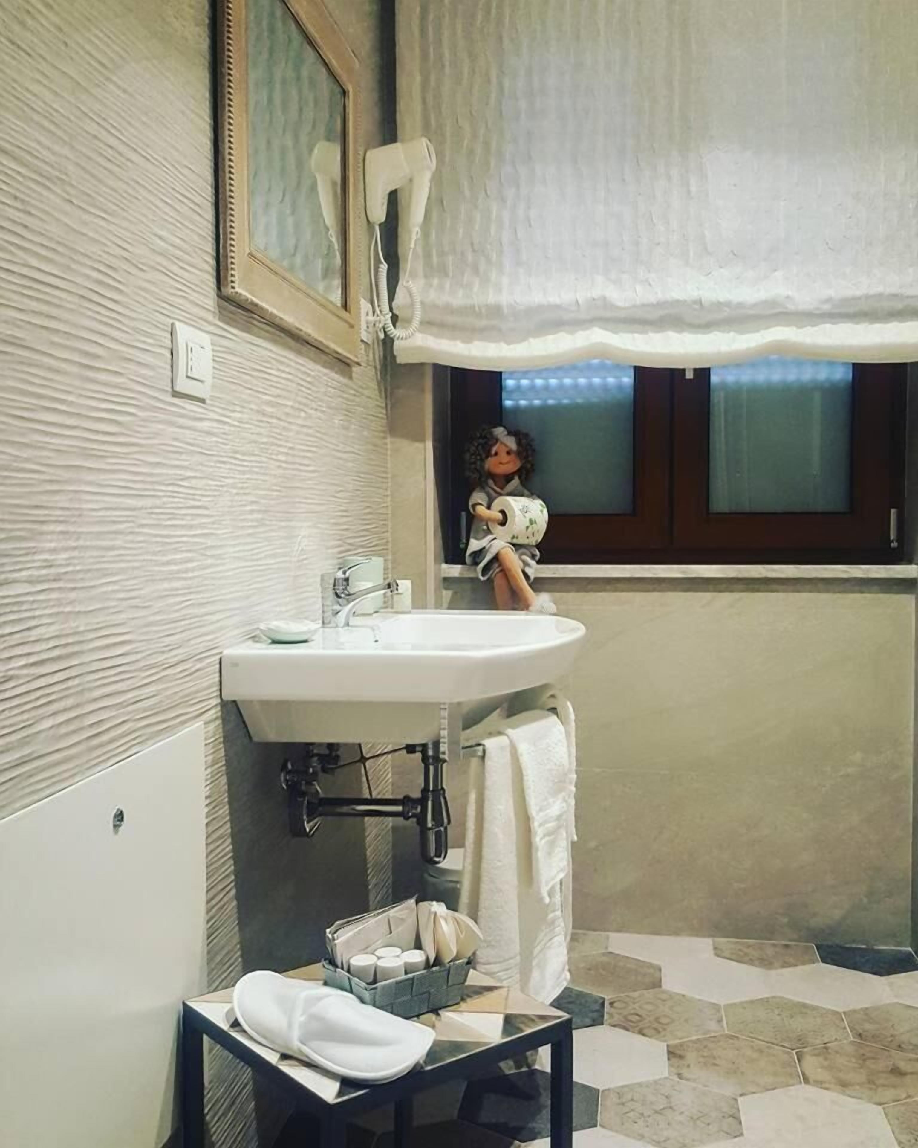 A bathroom with a sink, a towel rack, a window with a view, and a decorative item resembling a doll.