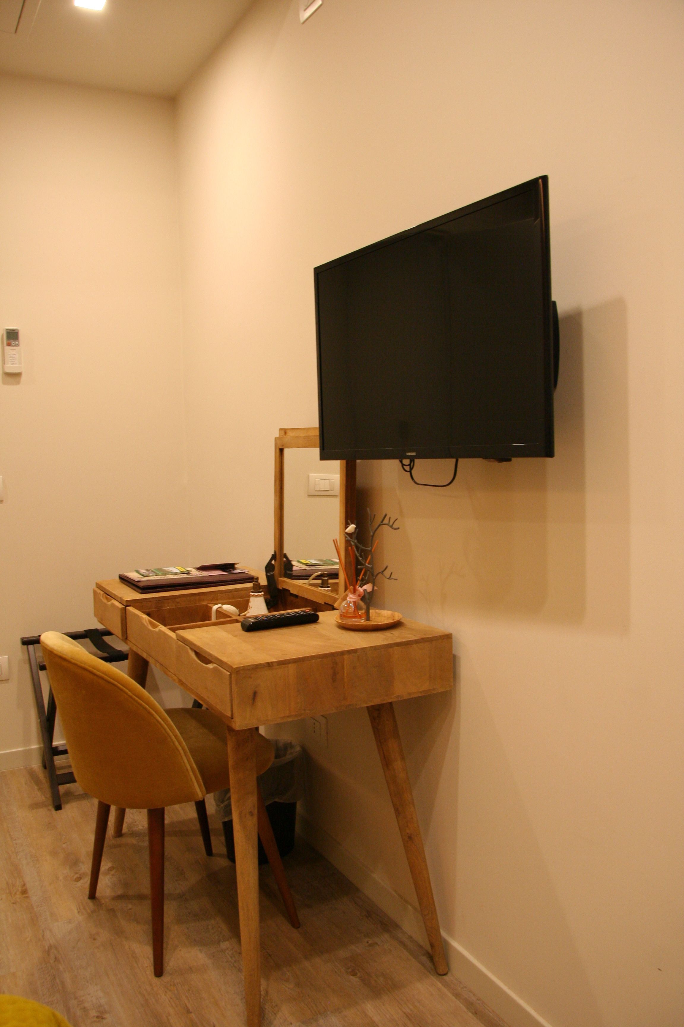 A compact room with a wooden desk, a chair, a television mounted on the wall, and a small decorative plant.