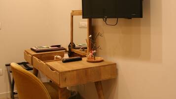 A compact room with a wooden desk, a chair, a television mounted on the wall, and a small decorative plant.
