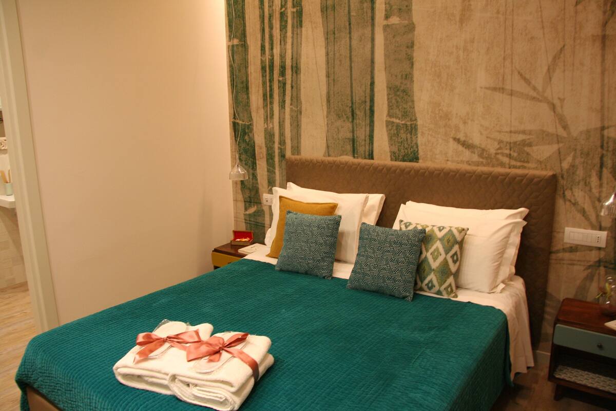 A neatly made bed with a green bedspread and a folded towel with a ribbon.
