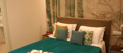 A neatly made bed with a green bedspread and a folded towel with a ribbon.