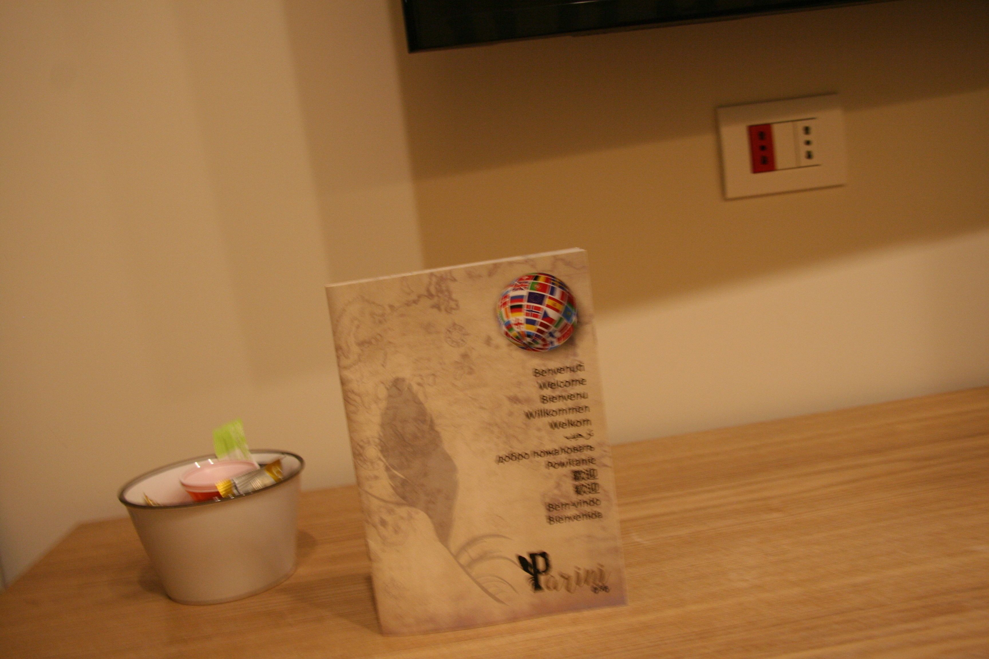 A welcome sign with multilingual greetings, a decorative globe, and a small trash bin on a wooden table.