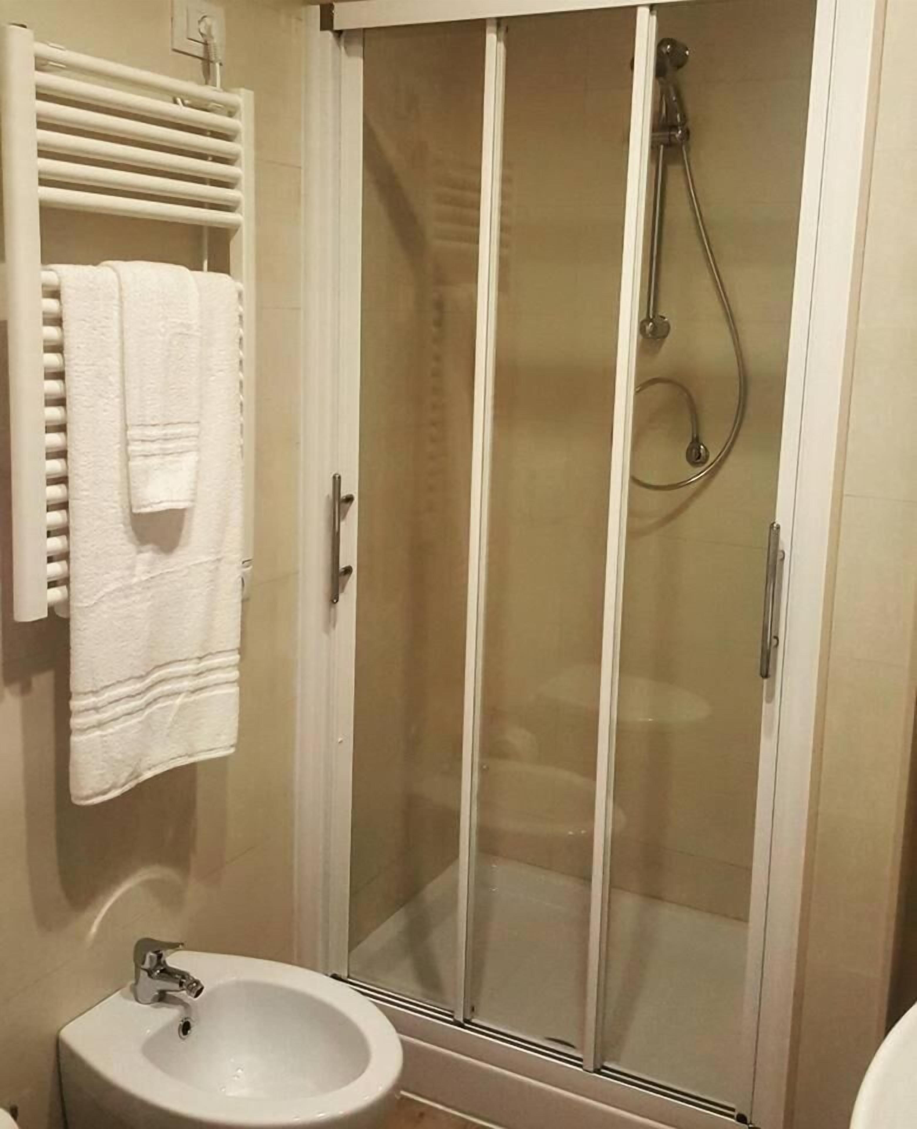 A bathroom with a glass-enclosed shower, a white sink, and a towel rack with a white towel.