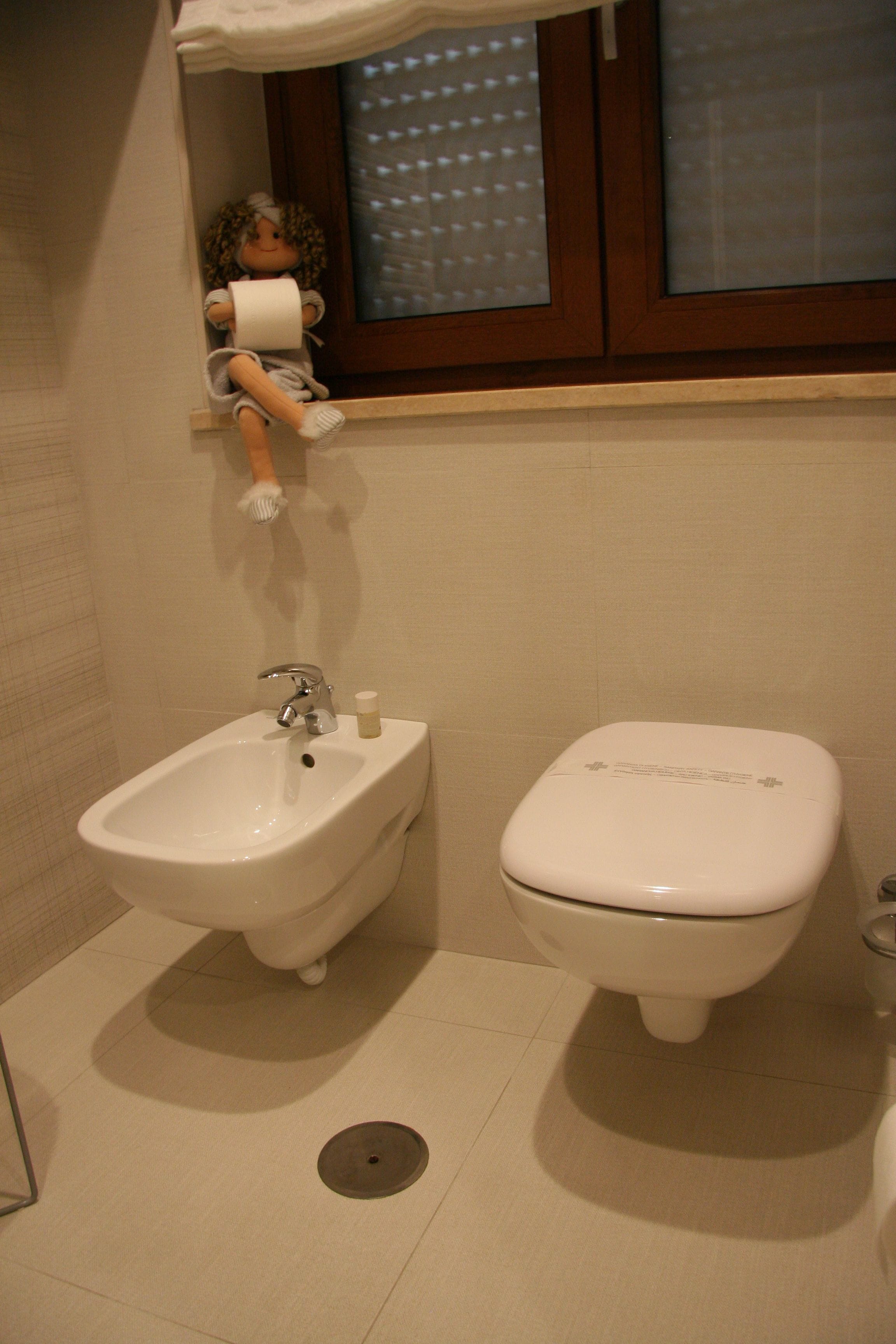 Een badkamer met een bidet, toilet, wastafel en een raam met zonwering.