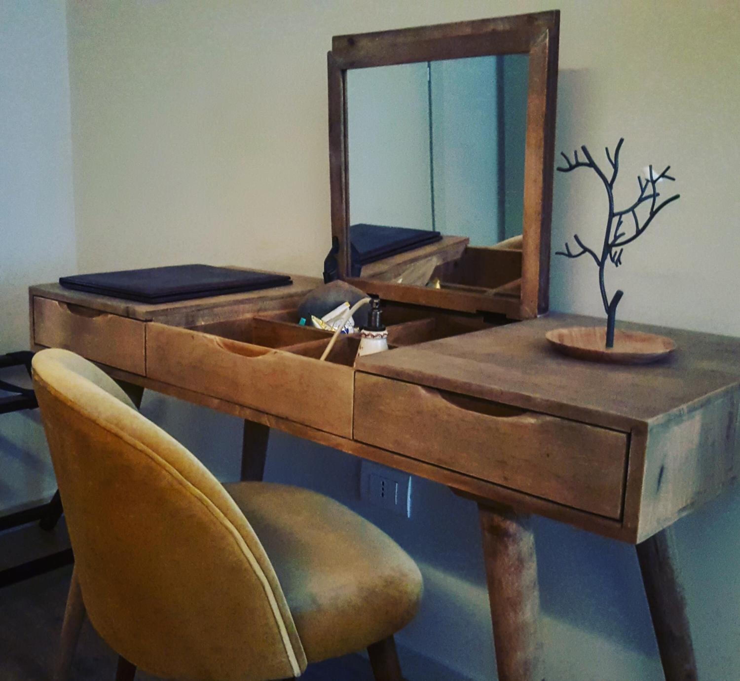 A wooden desk with a mirror, a small tree sculpture, and a chair.