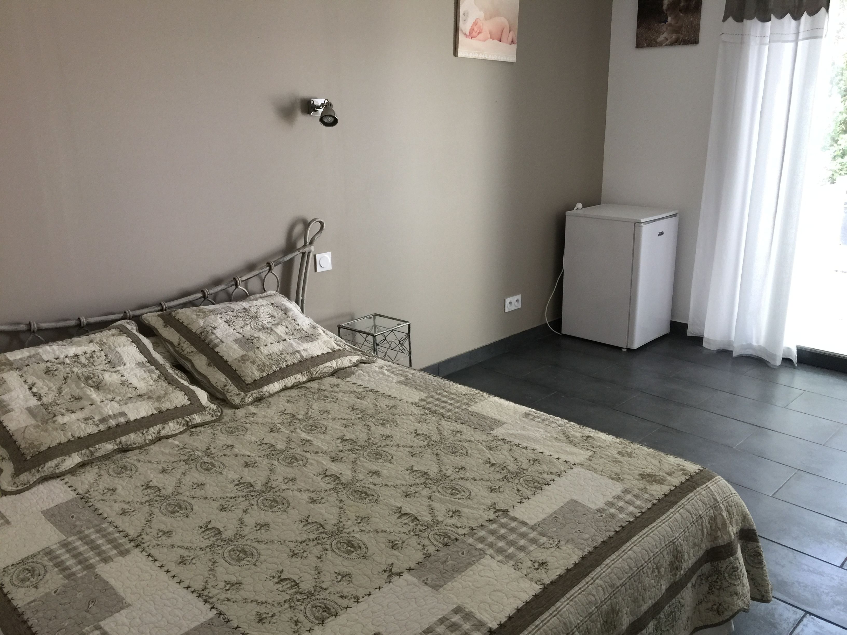 A bedroom with a bed, a small white cabinet, and a window with curtains.