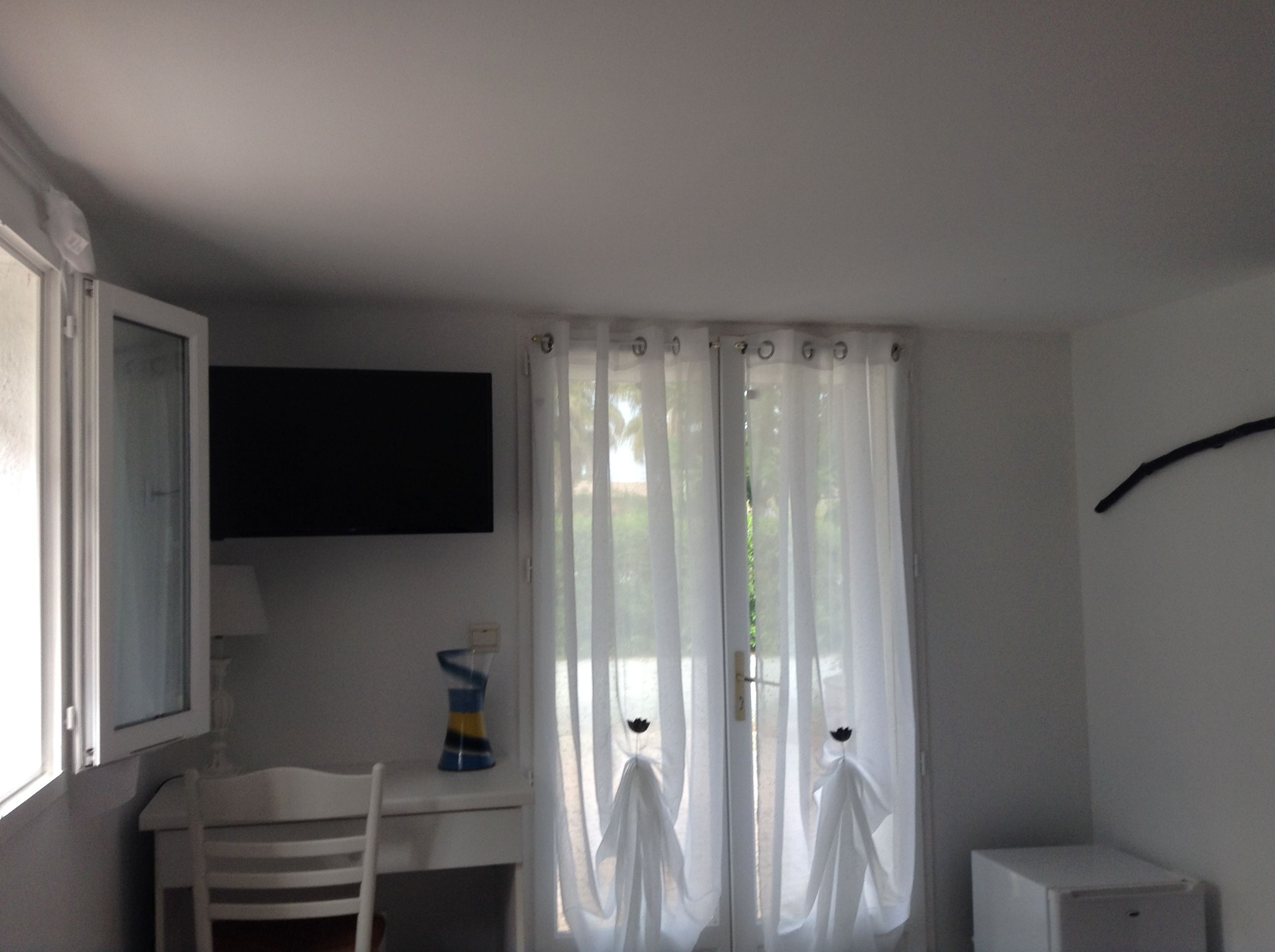 Une petite pièce simple, avec un bureau, une chaise et un meuble blanc.