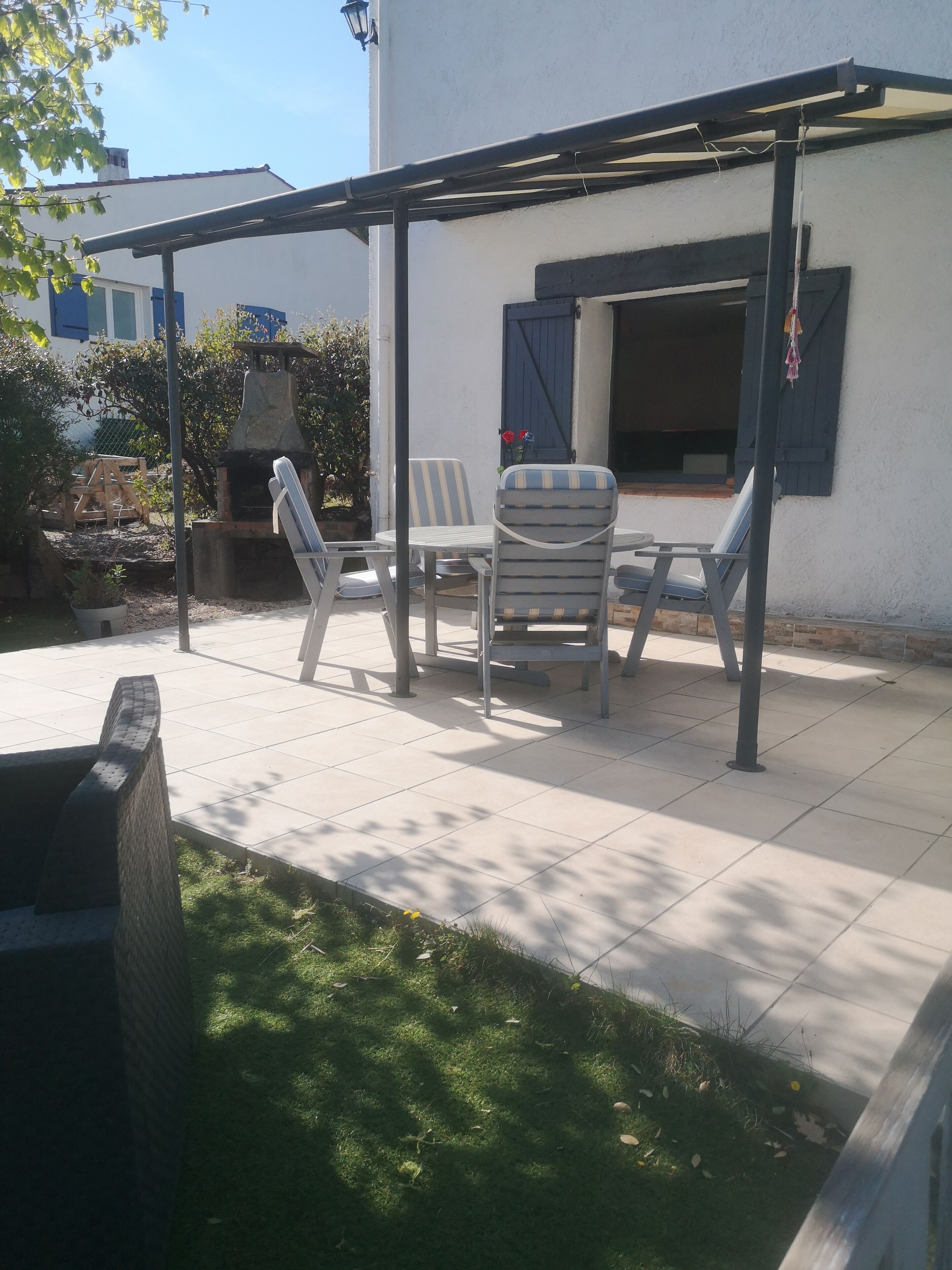 An outdoor patio with a pergola, a grill, and a seating area with chairs and a table.