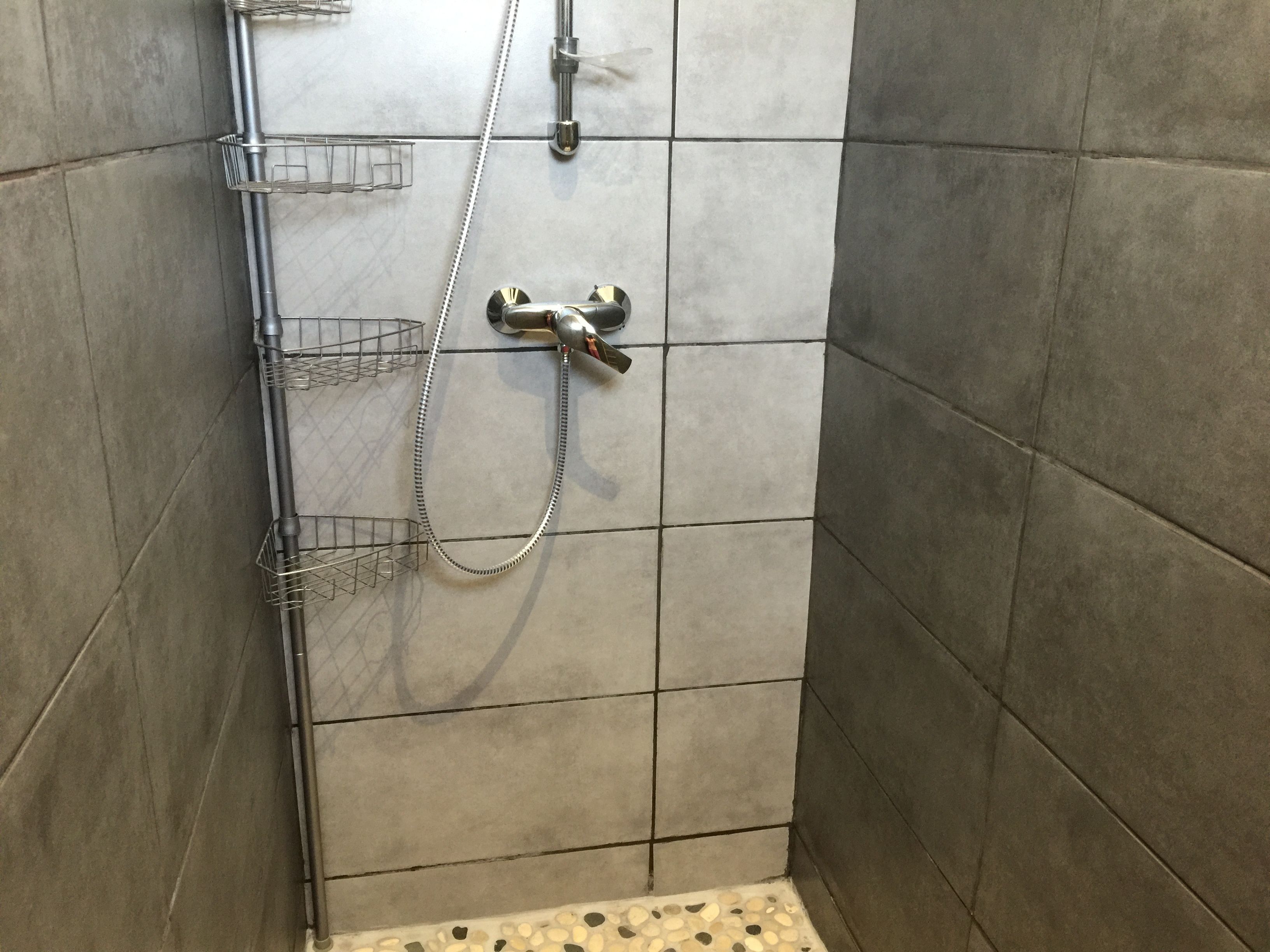 A shower area with a handheld showerhead, a wall-mounted faucet, and a metal shelf with hooks.