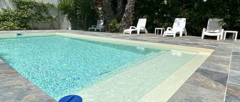 Une piscine rectangulaire à l’eau claire, entourée d’une terrasse carrelée et de chaises longues blanches.