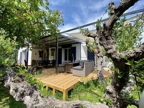 A covered patio area with outdoor furniture, a wooden deck, and a view of the surrounding garden. - Le Mas Du Bijou Bleu (Puget-sur-Argens)