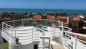 Eine Dachterrasse mit weißer Brüstung, einer Holzdielenfläche und Blick auf das Meer sowie Gebäude in der Ferne.