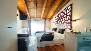 Habitación de hotel con techo de madera, cama con ropa blanca, mesita de noche con lámpara y baño con lavabo y espejo.