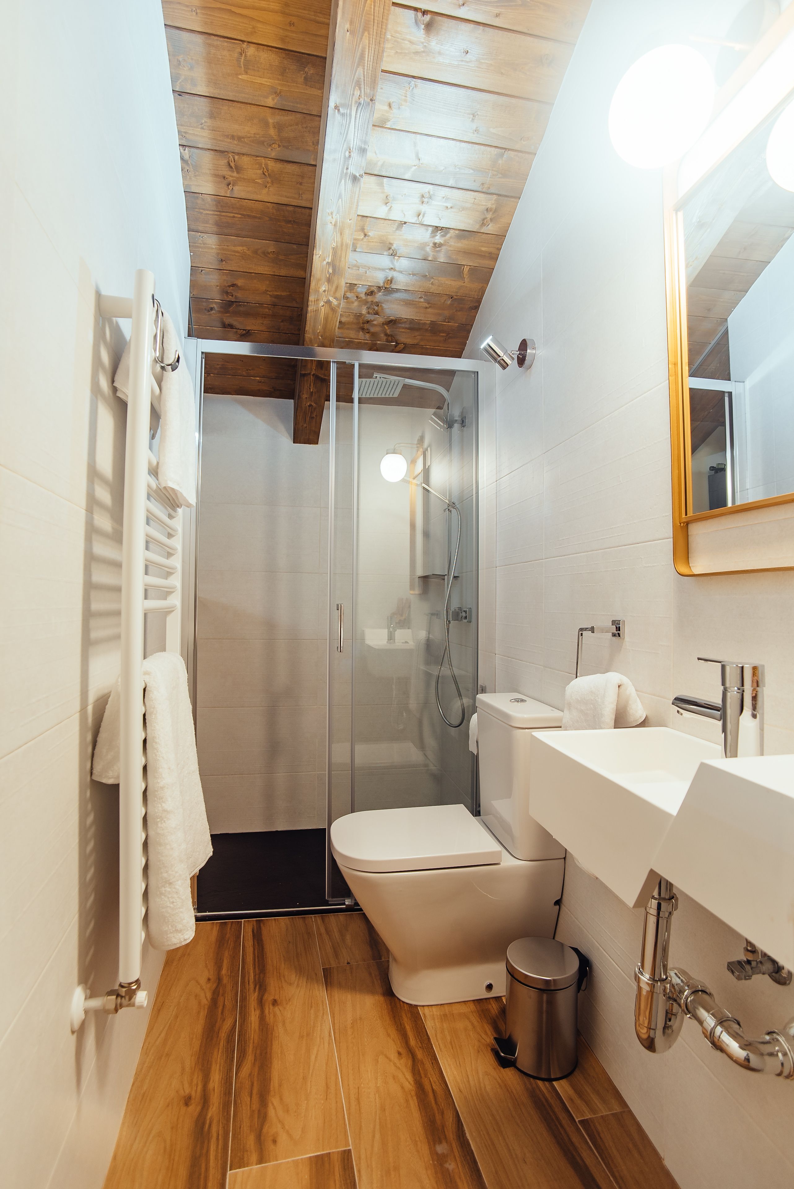 A bathroom with a shower, toilet, sink, and wooden floor.