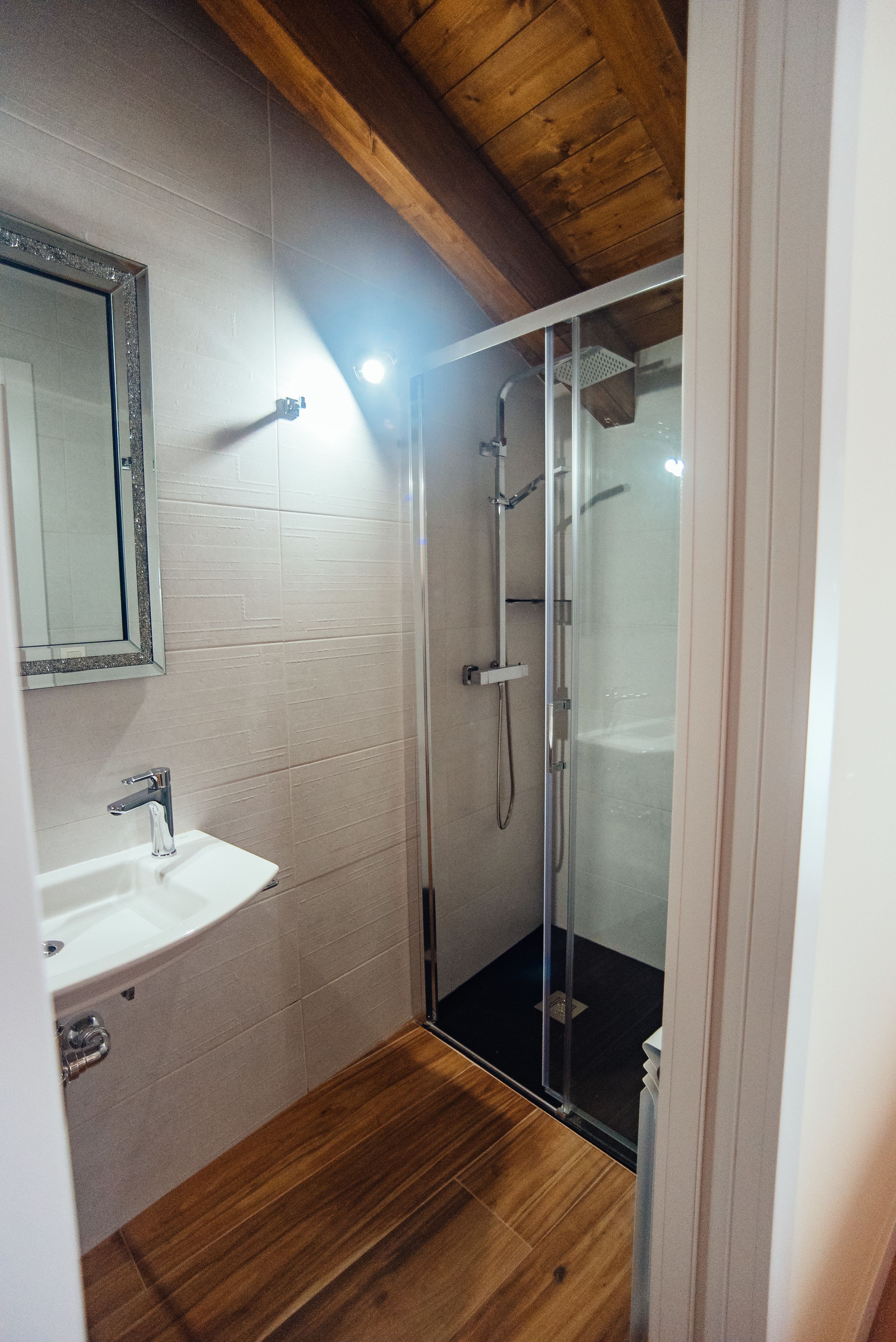 Un baño con cabina de ducha de vidrio, un lavabo blanco y suelo de madera.