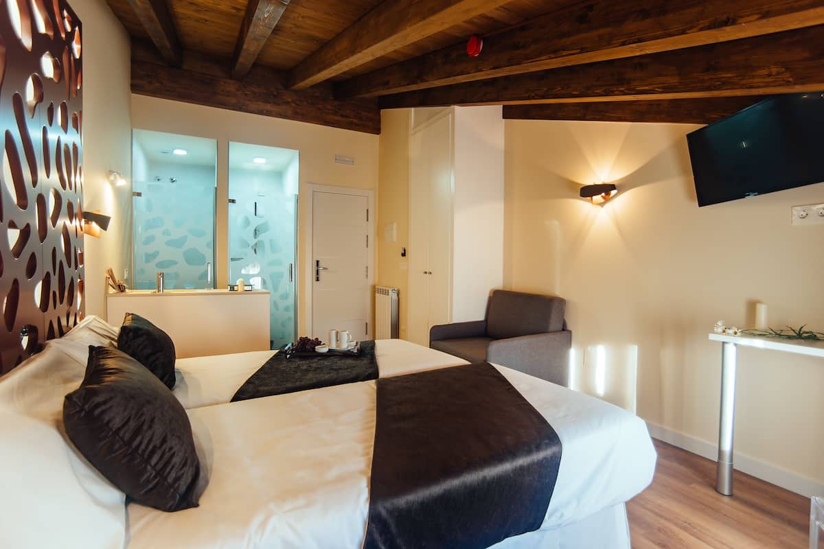 Habitación de hotel con una cama grande, un sofá, un televisor montado en la pared y una pequeña mesa con una vela.