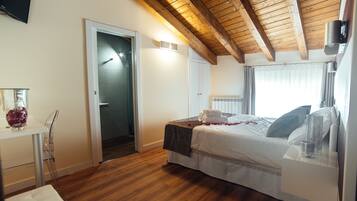 Camera da letto con soffitto in legno, un letto con lenzuola bianche, un comodino con un bicchiere e una porta che dà su un'altra stanza.