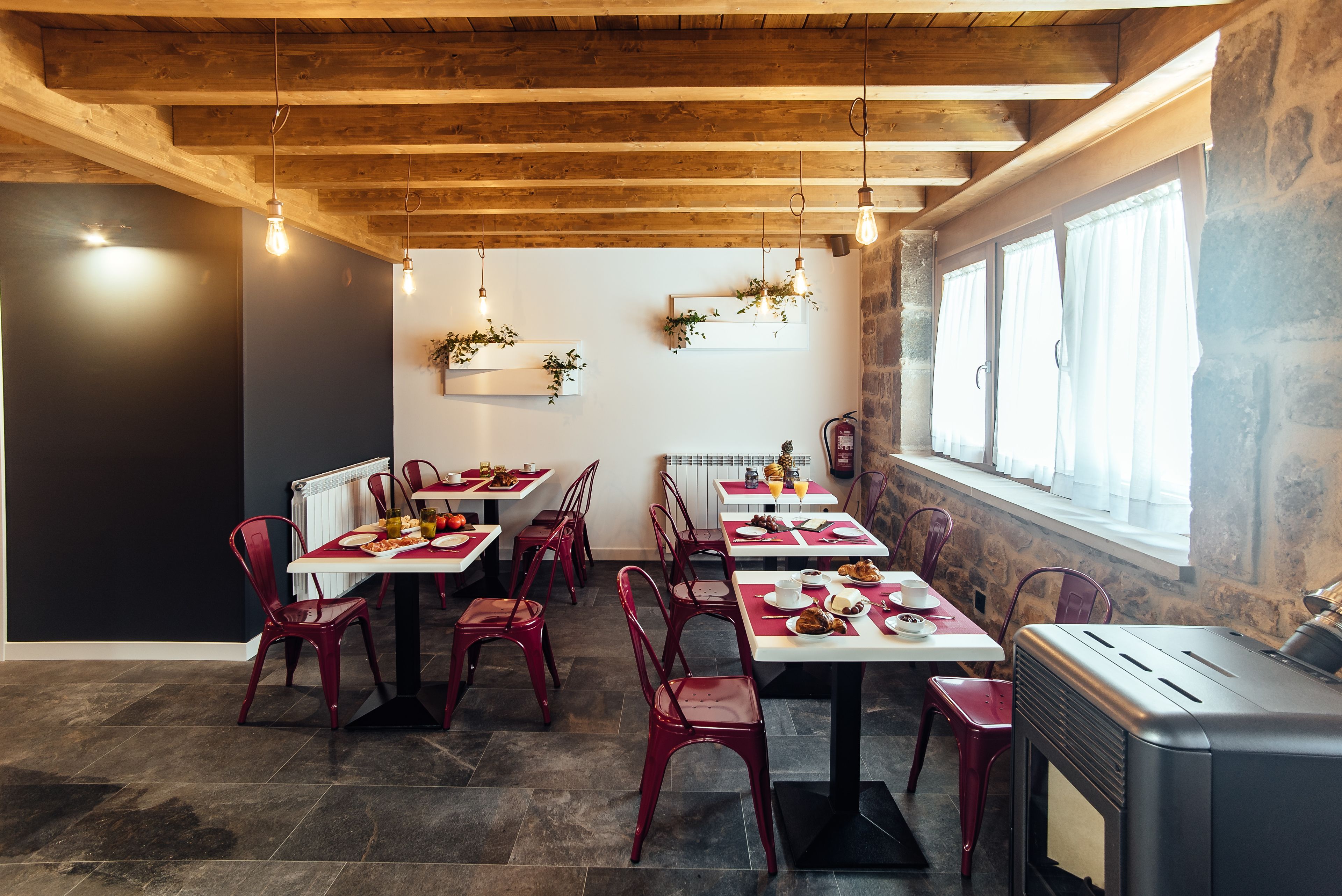 A restaurant with wooden ceiling beams, red chairs, and white tables.