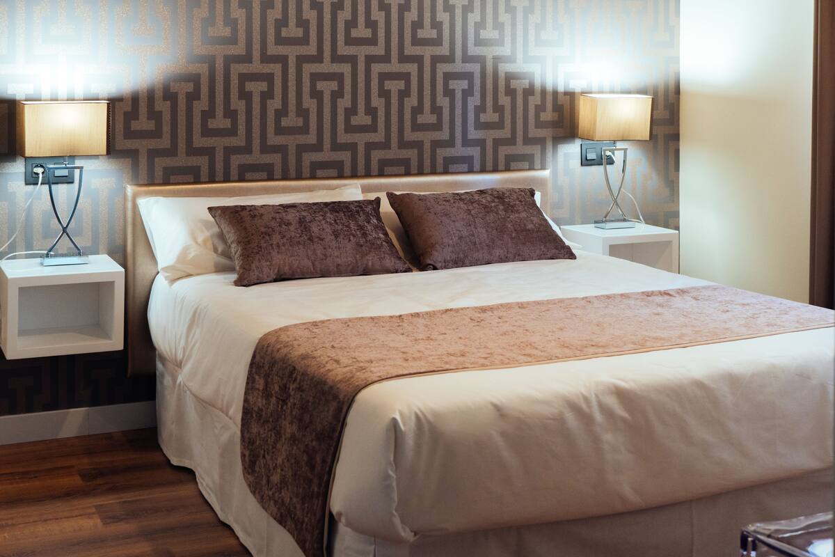 Una cama bien hecha con un cabecero estampado, dos lámparas de noche y un suelo de madera.