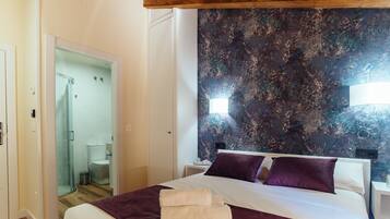A hotel room with a bed, a nightstand, a wall with a textured mural, a shower area, and a door leading to another room.