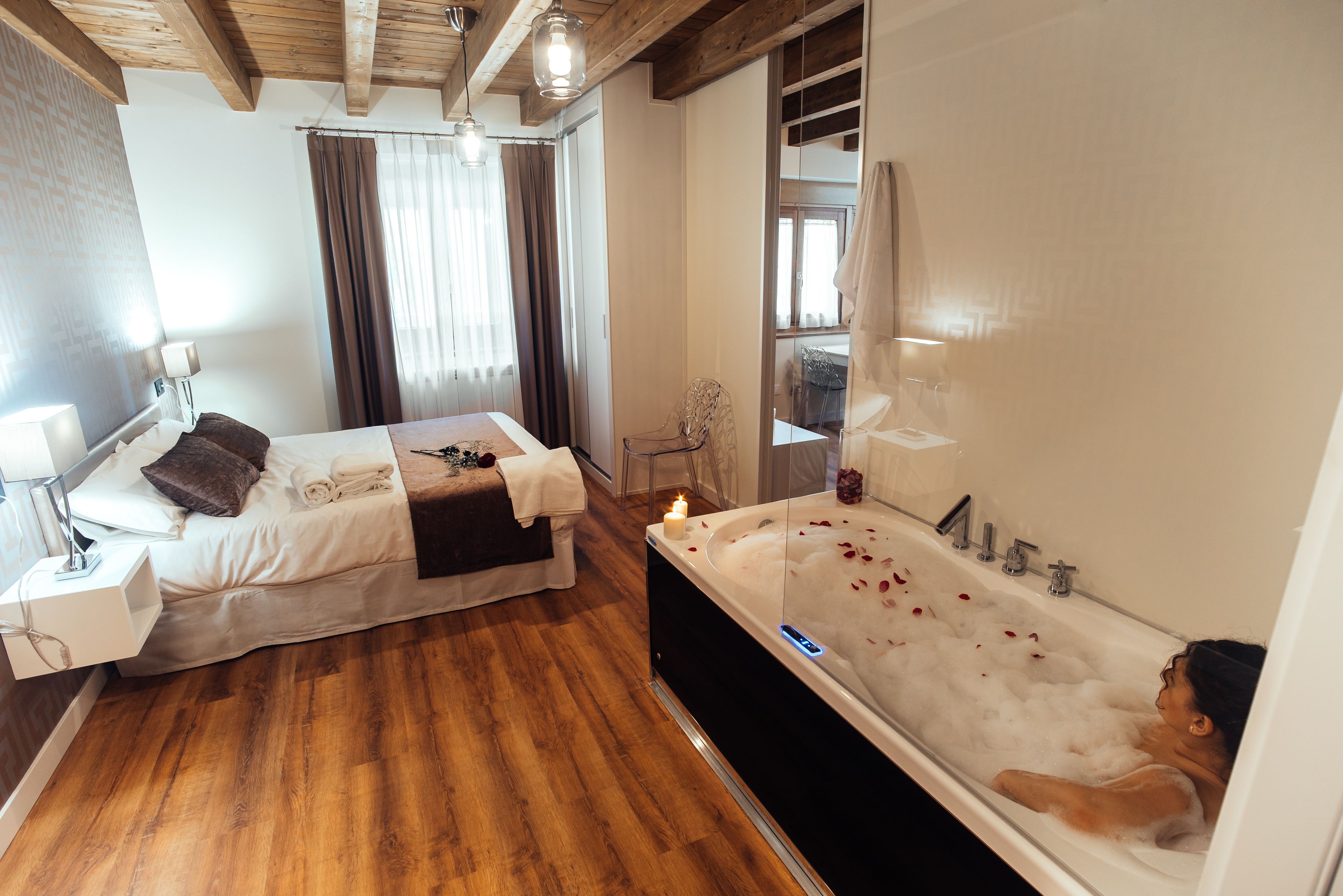 Un dormitorio moderno con una cama grande, una zona de estar separada y una bañera con pétalos de rosa.