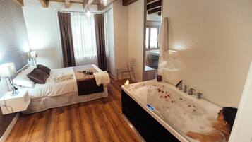 Un dormitorio moderno con una cama grande, una zona de estar separada y una bañera con pétalos de rosa.