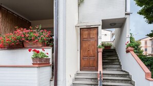 Un escalier menant à une porte en bois, avec des plantes en pot sur le palier.