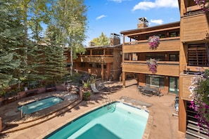 A two-story wooden building with a pool area, outdoor seating, and hanging flower baskets. - Aspen Condo w/ Pool, Hot Tub & 2 Blocks to Gondola - FH4 by RedAwning (Aspen)