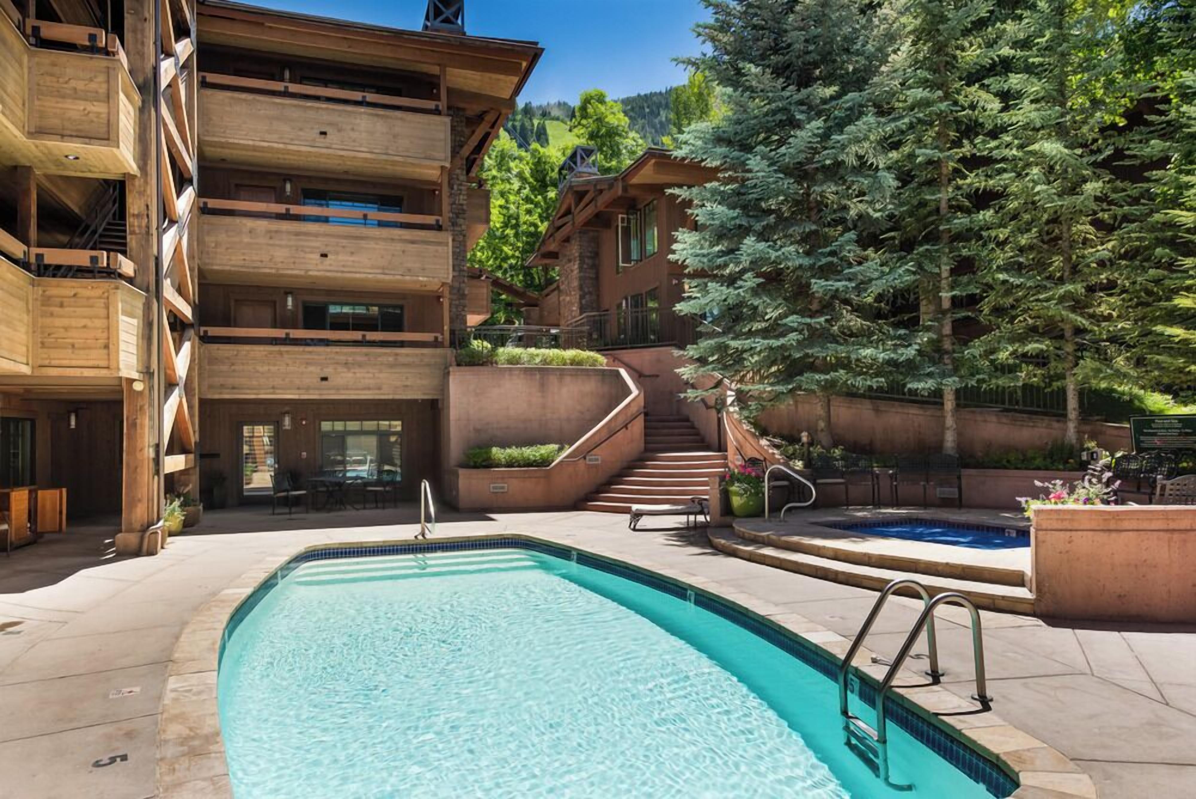 A modern building with a swimming pool, outdoor seating, and a staircase leading to a second floor.