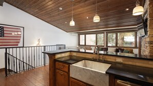 Cozinha com vigas de madeira no teto, uma janela grande e uma pia com bancada de mármore.