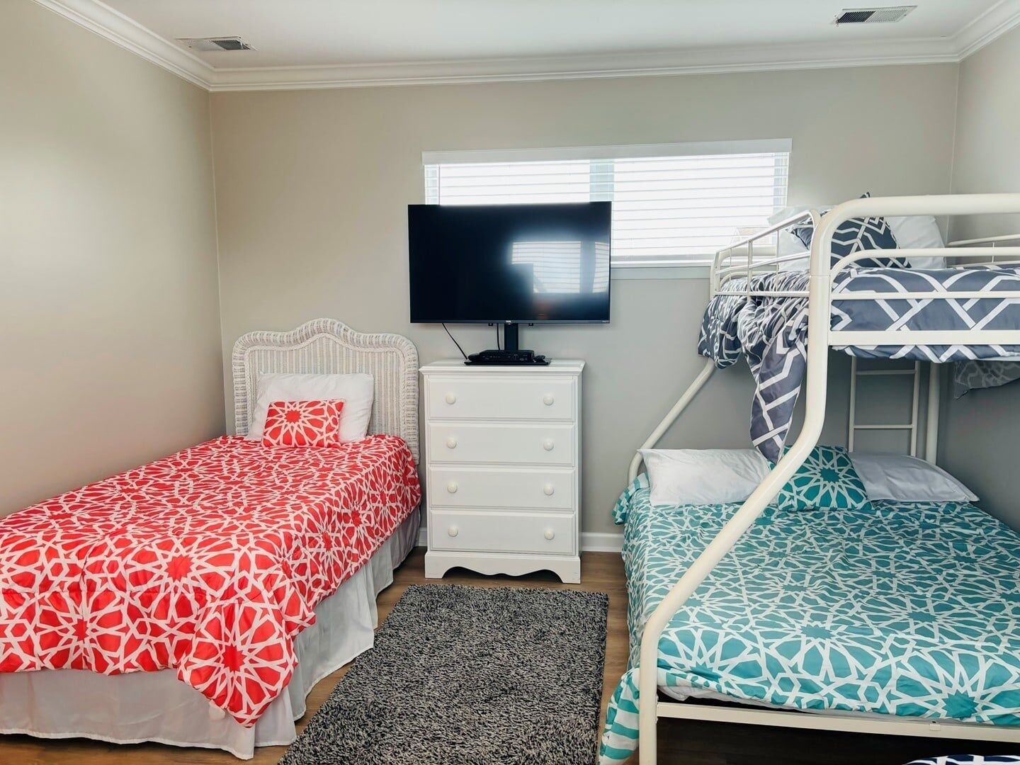Quarto com uma cama de solteiro, uma cama beliche, uma televisão e um armário.