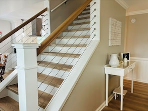 A staircase with wooden steps and white railings, leading to a landing with a small table and a chair. - Buckeye's At The Beach 3 Bedroom Home by RedAwning (Supply)