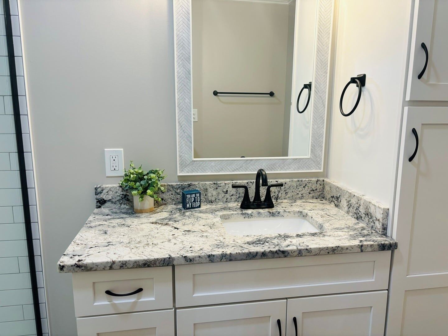A bathroom with a marble countertop, a sink, a mirror, and a potted plant.
