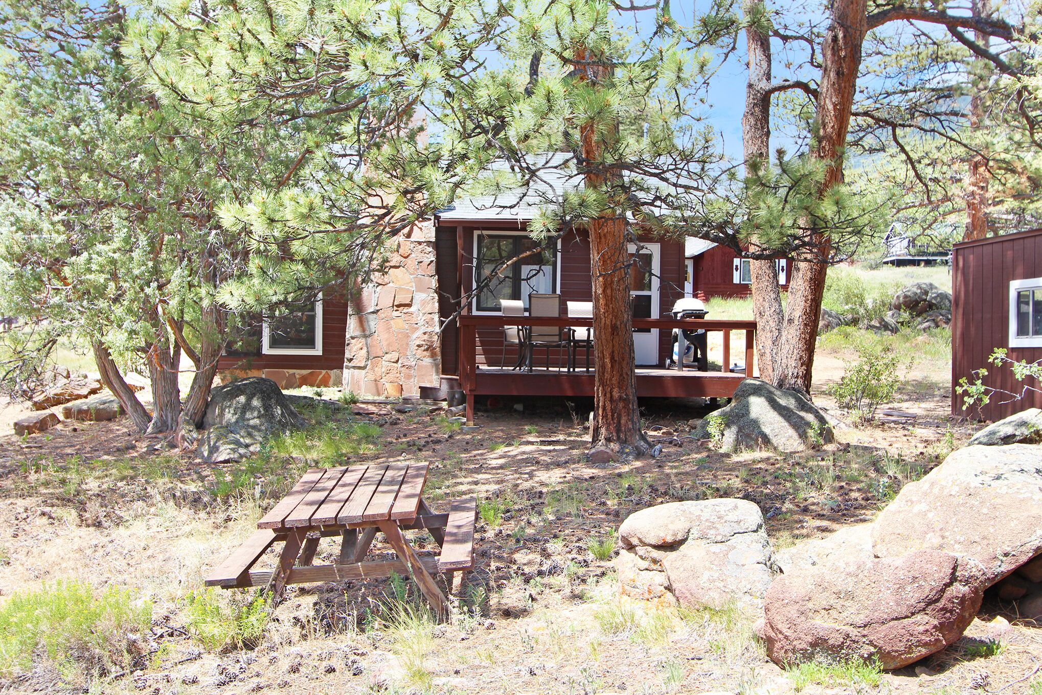 A rustic cabin with a wooden deck, surrounded by large trees and rocks.