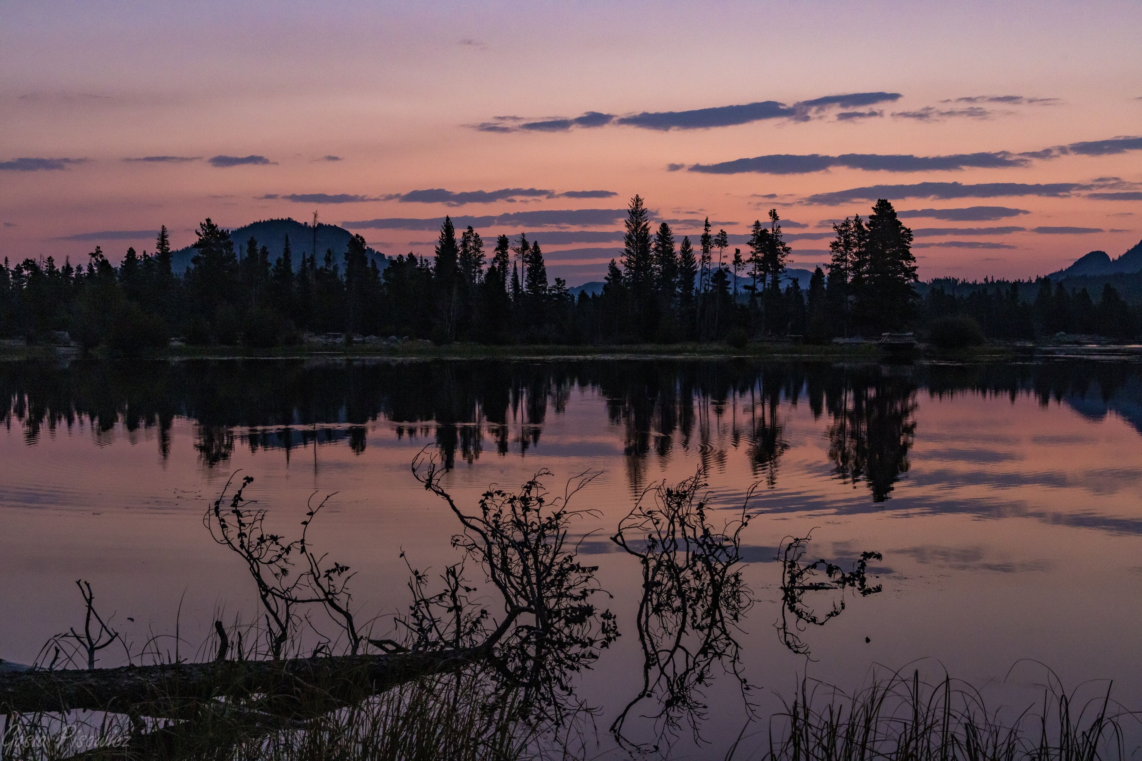Um lago calmo com reflexos de árvores e montanhas ao crepúsculo.
