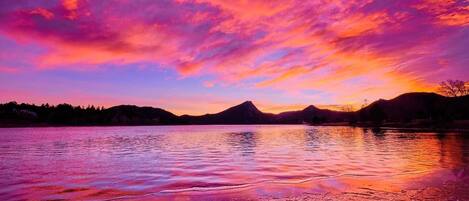 A lake with a sunset, mountains in the background, and a clear sky.