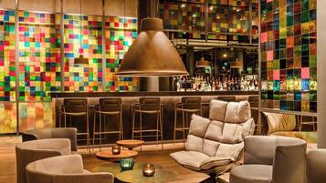 A modern lounge area with a bar, cushioned seating, and a colorful mosaic wall.