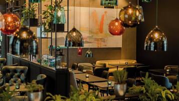 Un área de lounge moderna con asientos de cuero, mesas, lámparas colgantes y plantas en macetas.