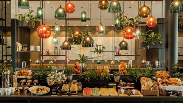 A buffet with various food items and a variety of hanging pendant lights. - Motel One Köln-Neumarkt (Cologne)