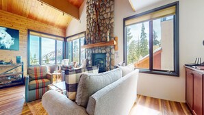 A cozy living room with a stone fireplace, large windows, and a wooden ceiling. - Bridges Townhome 5 Large, Remodeled Mountain View Townhome with Private Jacuzzi, Steps to Eagle Lodge by RedAwning (Mammoth Lakes)