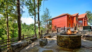 A red building with a stone fire pit in a forested area.