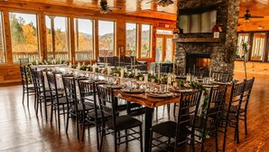 A long dining table set for a formal event with chairs, candles, and a stone fireplace.