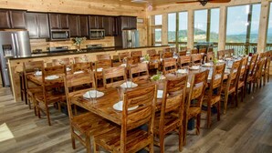 A spacious wooden dining area with multiple tables and chairs, a kitchen with modern appliances, and large windows offering a view of the outdoors. - Mansion In The Sky 11 Bedroom Cabin by RedAwning (Gatlinburg)