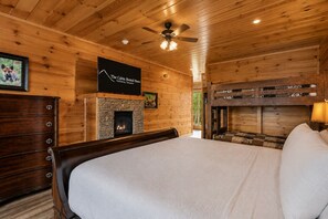 A cabin-style room with a stone fireplace, a bed with a white comforter, wooden walls, and a ceiling fan. - Mansion In The Sky 11 Bedroom Cabin by RedAwning (Gatlinburg)