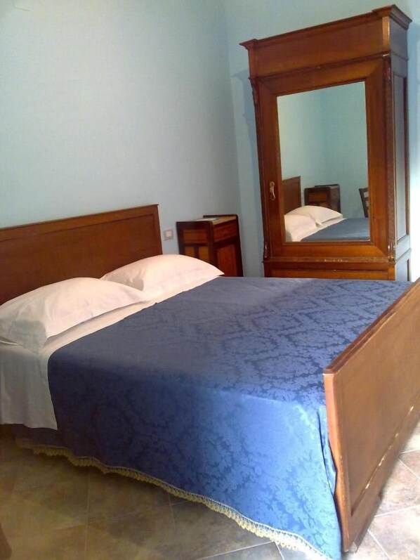Un dormitorio con cama de madera, una mesita de noche, un espejo y una colcha azul estampada.