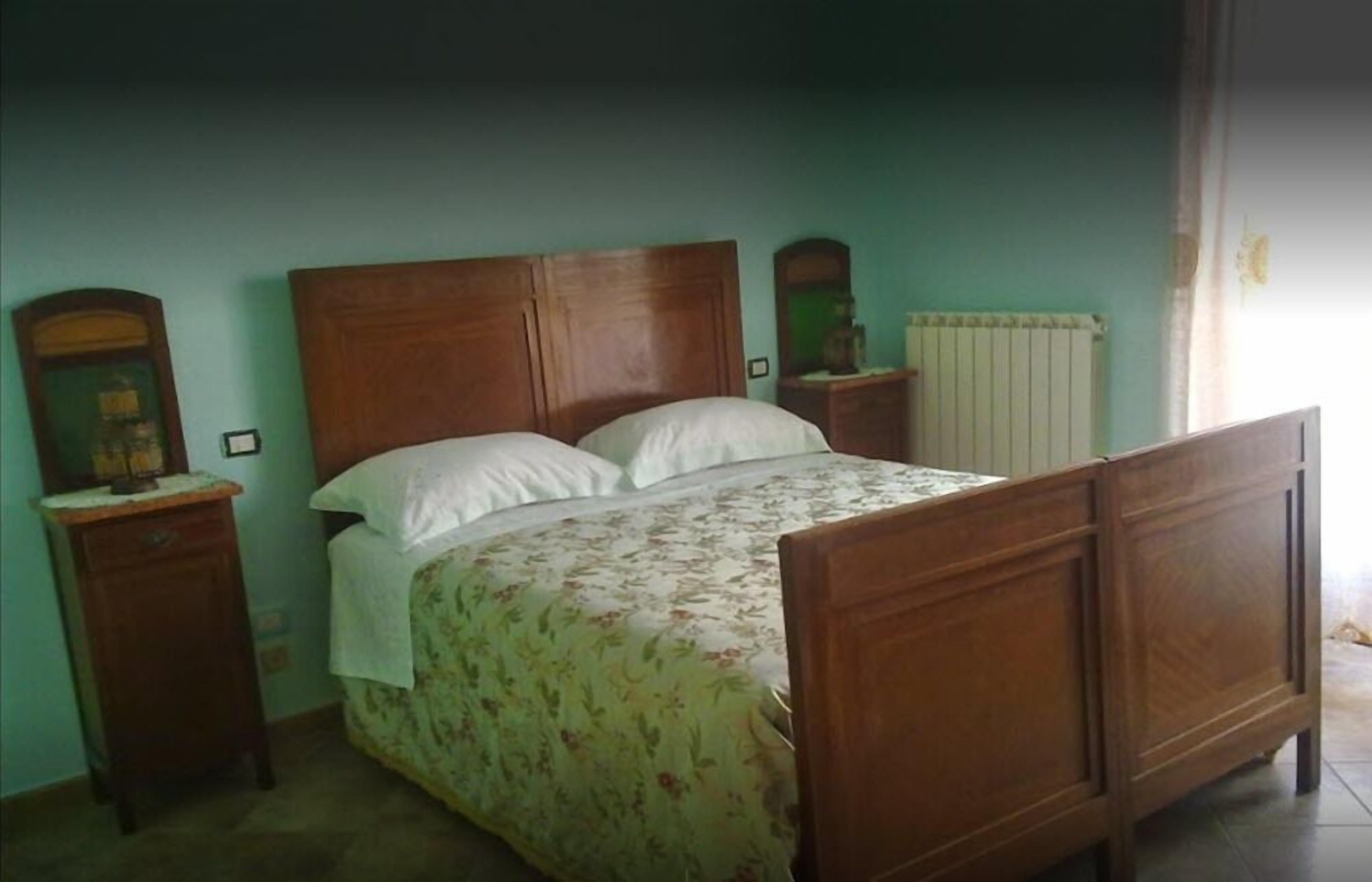 Une chambre à coucher avec un lit en bois, une couvre-lit à motifs floraux, deux tables de chevet et un radiateur.