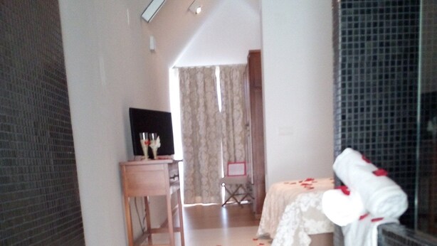 A hotel room with a shower area, a small table with a chair, and a bed with a white cover. - Hotel La Alcoholera (Villaviciosa de Córdoba)