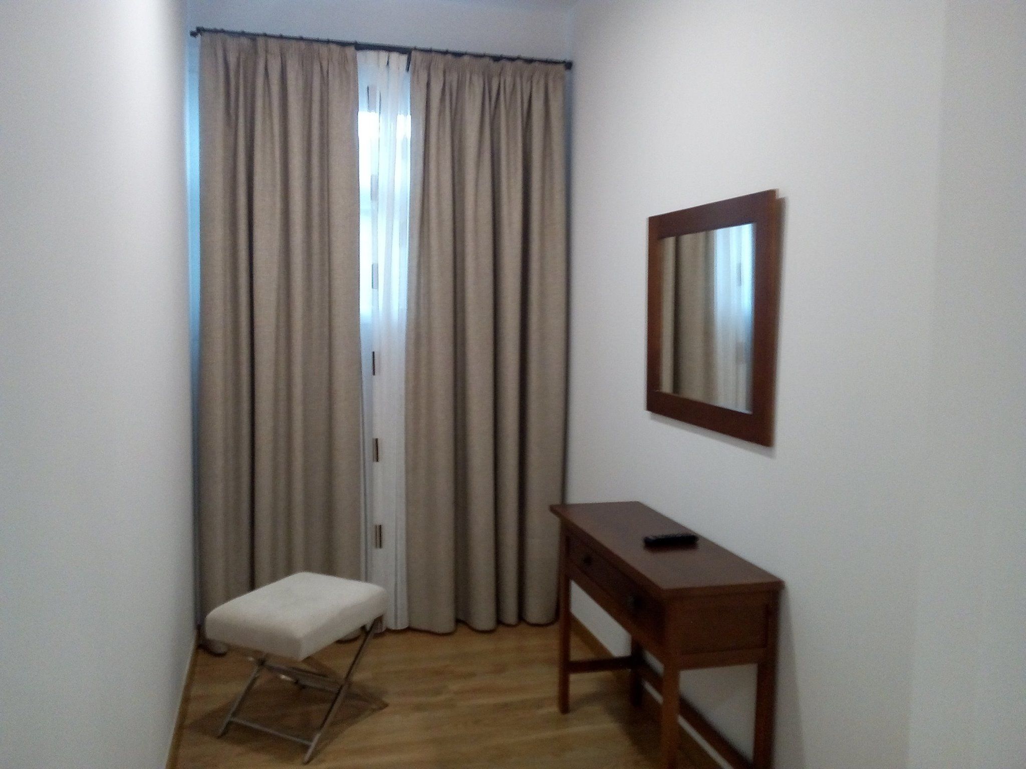 A room with a wooden floor, a small white bench, a wooden desk, and a mirror on the wall.